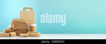 Eco friendly shopping, packaging and delivery banner. Craft cardboard gift boxes, paper bag and cardboard cups on blue background with copy space. Zer Stock Photo