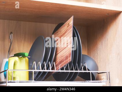 Crockery (mugs, cups, knife, cutting board, plates) on a dryer in a kitchen cabinet Stock Photo