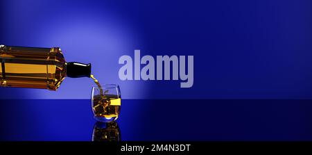bottle of whiskey / brandy being poured pouring into a glass with ice cubes scotch on the rocks backlit against a blue background Stock Photo