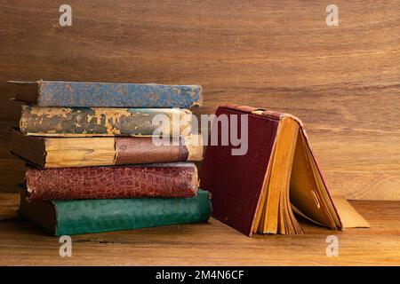 Side view stack of old torn hardcover books on wooden table. Old grungy books on wooden baclground. Stock Photo