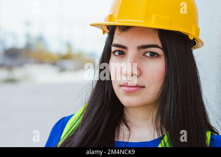 portrait of young caucasian female engineer wearing protective helmet and safety vest, smiling looking at camera, engineering concept, copy space. Stock Photo