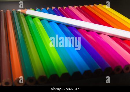 Detail of some wooden pencils of multiple colors ordered by color like the rainbow, on all of them the white pencil stands out Stock Photo