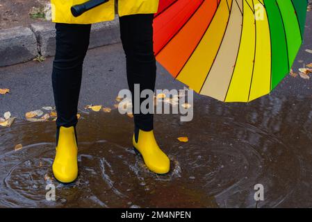 the multi-colored umbrella and yellow boots in a puddle Stock Photo