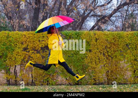 a girl with a multi-colored umbrella jumps in the park Stock Photo