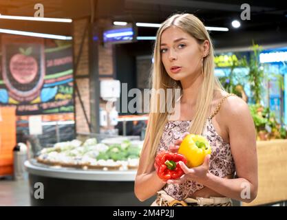 Selecting freshness and quality. Beautiful young women holding red and yellow pepper and smiling while standing in a food store Stock Photo
