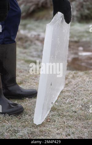 A teenage boy removes a thick piece of ice from a frozen lake during the recent cold weather in the new forest Hampshire UK. Stock Photo