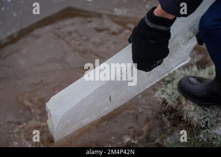 A teenage boy removes a thick piece of ice from a frozen lake during the recent cold weather in the new forest Hampshire UK. Stock Photo