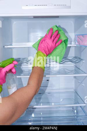 Cleaning empty refrigerator - woman's hands in gloves holding cleaning rag and spray detergent Stock Photo
