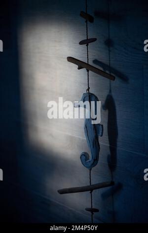 Beautiful window light hitting a grey tiled bathroom wall with a blue seahorse wooden rope ornament hanging down with copy space. Stock Photo