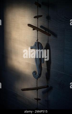Beautiful window light hitting a grey tiled bathroom wall with a blue seahorse wooden rope ornament hanging down with copy space. Stock Photo