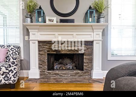 A white wood fireplace in a new home with windows and a chair in a living room Stock Photo