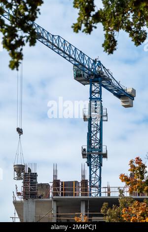 Blue high crane working on concrete construction site on cloudy sky background Stock Photo