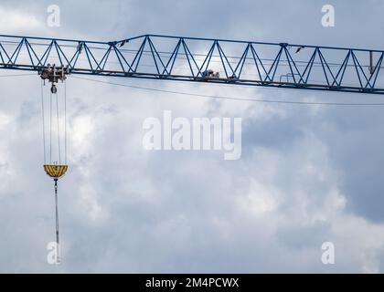 Blue tall crane projecting arm for lifting heavy weights on construction site on cloudy scenic sky background Stock Photo