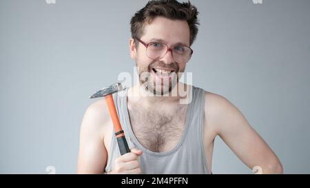 Mad repairman concept. Builder repairman, foreman holding hammer in hand, looking with vrazy grimace. DIY concept. Stock Photo