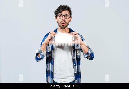 Surprised guy in glasses showing blank screen of smart phone. Amazed young man showing ad on cellphone. Surprised handsome man showing the horizontal Stock Photo