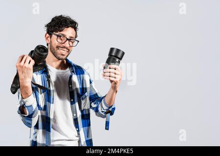 Portrait of smiling photographer man showing a camera and lens on isolated background. Smiling young man holding a camera isolated, Smiling Stock Photo