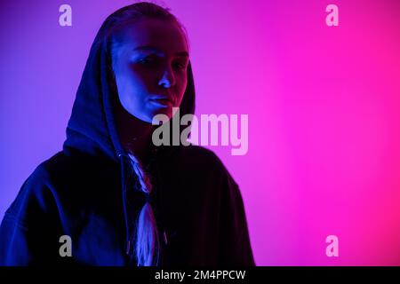 Colorful low-key portrait of a cool and confident blonde woman in hoodie Stock Photo