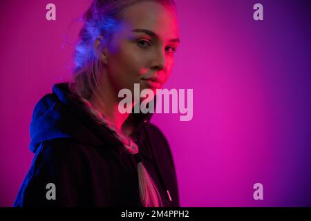 Colorful low-key portrait of a cool and confident blonde woman in hoodie Stock Photo