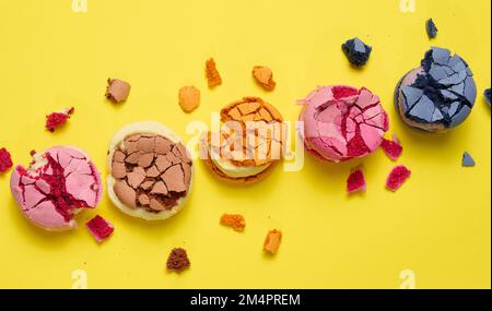 Broken round macarons with crumbs on a yellow background, delicious dessert, top view Stock Photo
