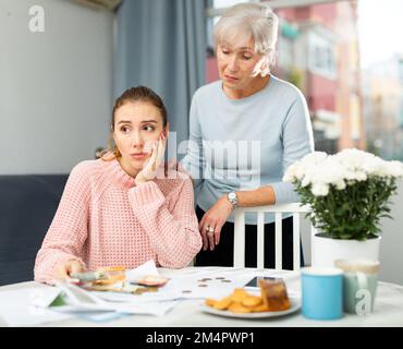 Upset young woman with elderly mother calculating running costs of household chores Stock Photo