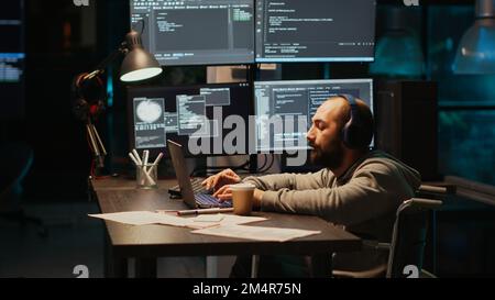 IT web developer writing source code in office, dealing with physical disability at night. Software engineer wheelchair user working late to develop new server database with html script. Stock Photo