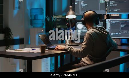 Software engineer typing programming code on laptop with multiple monitors, working with html script on terminal window. Developing algorithms and online cloud computing late at night. Stock Photo