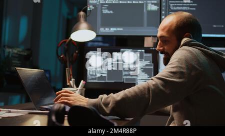 Database admin answering landline phone call late at night, talking on office telephone with cord and typing source code. Creating algorithm for company agency, writing html script. Handheld shot. Stock Photo