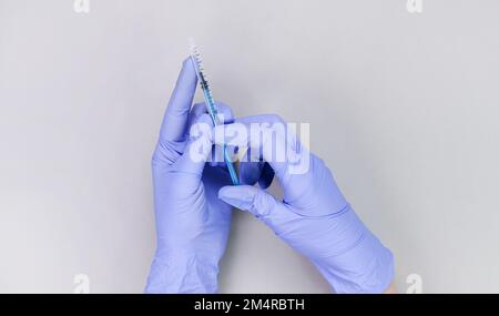 Hands in blue gloves of doctor or nurse holding syringe with liquid vaccine over grey background with copy space. New vaccine. Unknown vaccine. Medica Stock Photo