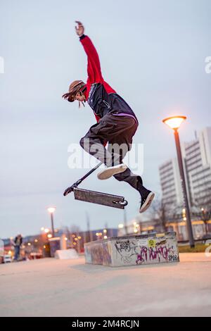 Wiesbaden, Germany - December 15, 2019: boy jumping with his push scooter at the skate park in the evening. Stock Photo