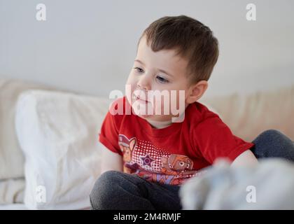 baby boy watching tv on the bed with face in strawberry juice Stock Photo