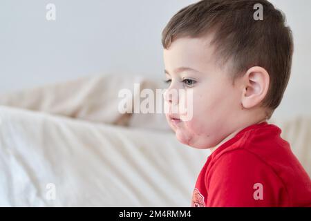 baby boy watching tv on the bed with face in strawberry juice Stock Photo