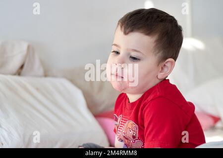 baby boy watching tv on the bed with face in strawberry juice Stock Photo