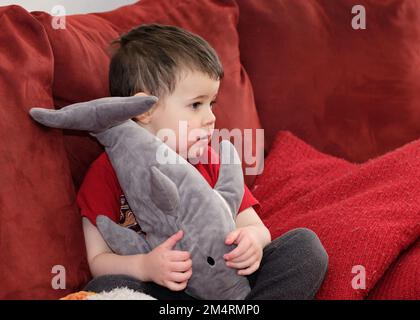 baby boy watching tv on the couch with face in strawberry juice Stock Photo