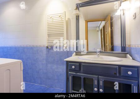 Bathroom with white porcelain sink with marble countertop and blue wooden cabinet with integrated mirror and sconces in the same color as the tiles Stock Photo