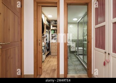 Bedroom with white wardrobe and dresser cupboard with drawers and shelves and bathroom with walk-in shower and green tiles Stock Photo