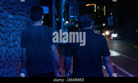 Two men walking on the side of a city highway at night and lit by a blue street lamp Stock Photo