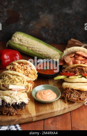 A closeup view of six differently flavored arepas served with sauce and a corn Stock Photo