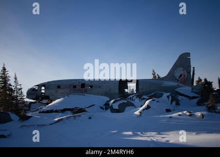 Miss Piggy Plane wreck in Churchill, Manitoba with blue background in frame with snow on rocks in front of crash landing site. Stock Photo