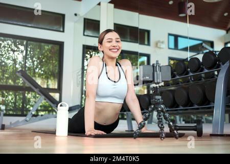 Young woman watching fitness video or having video conference with fitness trainer at smartphone screen. Stock Photo