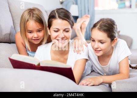 Woman reading book to daughters on sofa Stock Photo