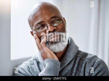 Hes thinking a few things through today. a handsome senior man looking thoughtful while sitting in his home. Stock Photo