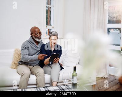 Just browsing the net trying to find videos we like. an affectionate senior couple using a tablet while relaxing on the sofa at home. Stock Photo