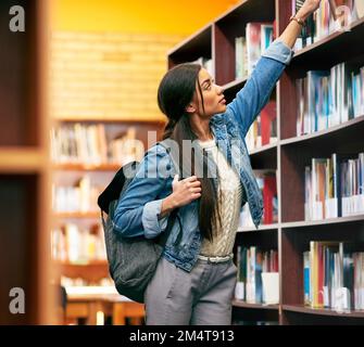 Getting through her reading list for campus. a university student looking for a book in the library at campus. Stock Photo
