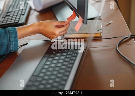 Close up of woman hand glues sticky stickers on computer while sitting at home office table Stock Photo