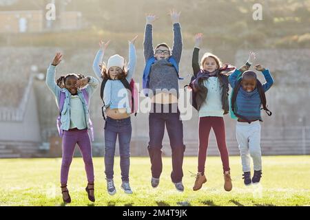 Schools out, time to have fun. elementary school kids jumping outside. Stock Photo