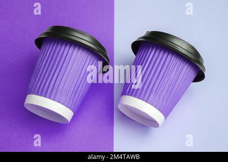 Close-up image of two purple paper cups for takeaway coffee or tea placed parallel and tilted to the right on a colorful designer table. Copy space. Soft selective focus Stock Photo
