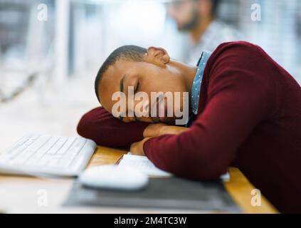Just going to close my eyes for a few minutes. a tired young man sleeping on a desk with his arms folded inside of a library. Stock Photo