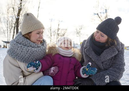 Grandmother, mother and daughter are walking in the winter city park on Christmas and New Year holidays. Parent and little child having fun outdoors Stock Photo