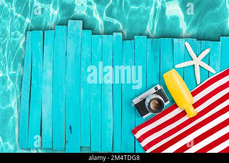 Red and white striped towel with camera, yellow bottle, starfish on blue wooden boards, pier. Pool, beach, sea. Vertical, horizontal. Vacation, travel Stock Photo