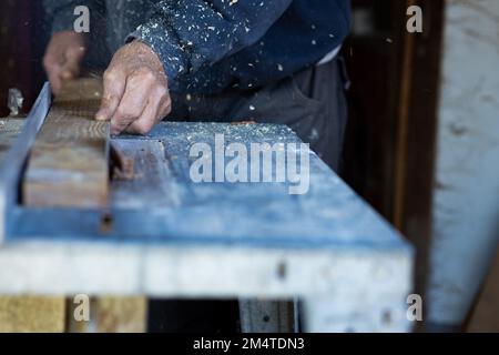 sawdust flies around as a worker,carpenter cuts a wooden batten on a circular saw. Close-up photo of a worker's hand holding a wooden lath Stock Photo